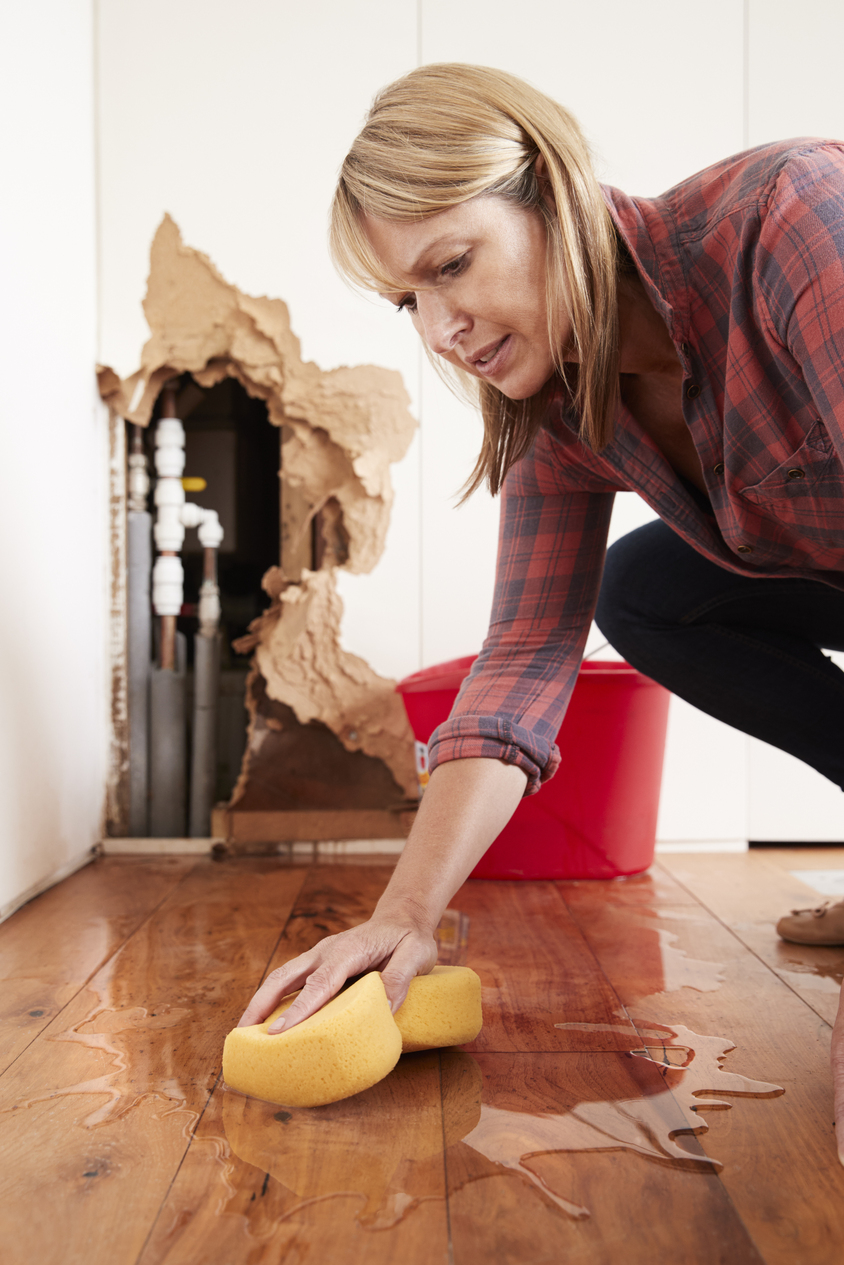 Homeowner dealing with burst pipe water damage on hardwood floor
